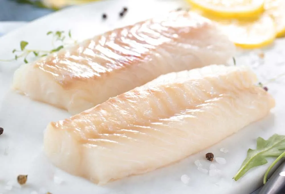2 raw cod fish fillets on a white plate with seasoning and ganish