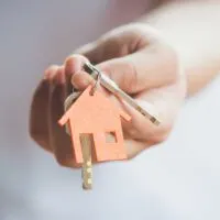 Hand holding out a set of keys with a small house key chain