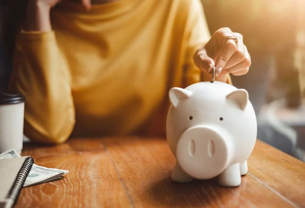 Person sitting at a table putting change into a piggy bank