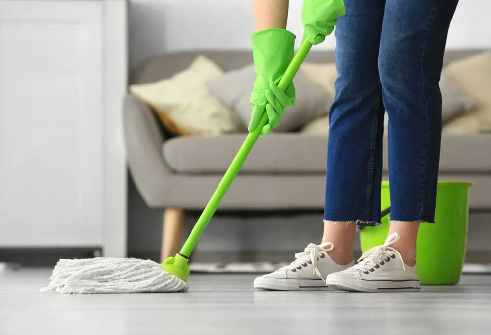 Lower half view of a person mopping the floor with a couch in the background