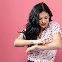 Woman standing in front of a pink background scratching her arm