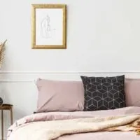 Bed made with mauve linens, a dark pillow with geographic shapes, with a small table next to the bed