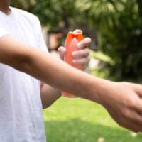person spraying bug spray on their arm