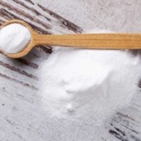 Pile of baking soda on a distressed wood surface next to a wooden spoon full of baking soda