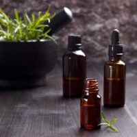 Brown essential oil bottles in front of a mortar and pestle full of rosemary on a wooden table