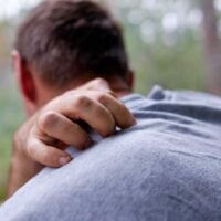 man with face turned away from the camera reaching back to scratch his shoulder