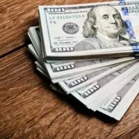 100 dollar bills spread out like a fan on a wooden table