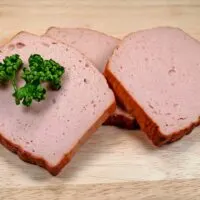 Sliced liver loaf on a cutting board with a parsley garnish