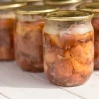 Glass jars of canned beef on a white wooden table.