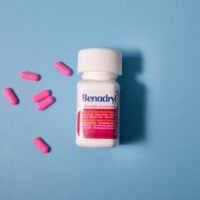 a Benadryl bottle laying on a blue background with pink pills spread around it.