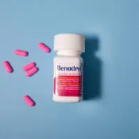 a Benadryl bottle laying on a blue background with pink pills spread around it.