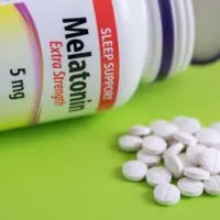 Bottle of Melatonin on its side on a green background with a pile of pills next to it