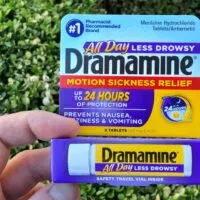 Person holding a package of Dramamine outdoors in front of shrubs