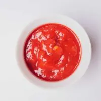 Overhead view of a bowl of tomato sauce on a white background.