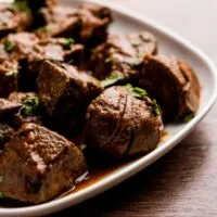 Chunks of cooked lamb liver on a white plate on a wooden table