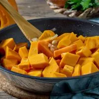 Diced pumpkin in a skillet being stirred with a wooden spoon
