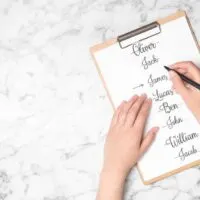 Clipboard holding a paper with full of boys names while hand holding a pin strikes through the names